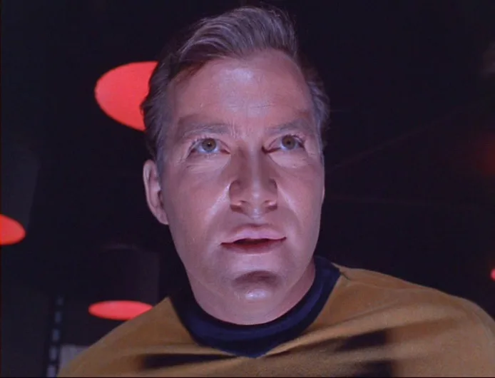 A close-up of actor William Shatner as Captain James T. Kirk from Star Trek, looking upward with a startled expression. He…