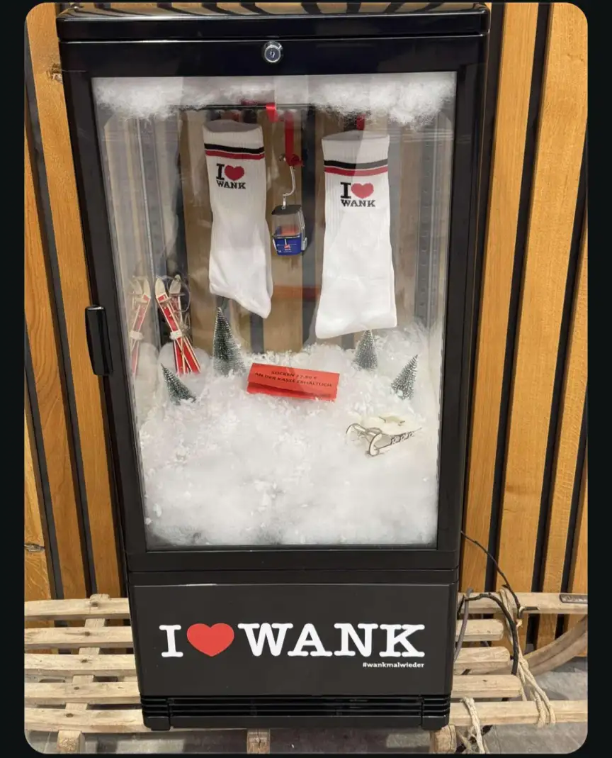 A black vending machine decorated with artificial snow, miniature Christmas trees, and ski equipment, displays two white…