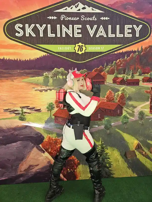 A person in a Fallout 76 Pioneer Scouts cosplay, wearing a red cap, white and red outfit, black boots, and holding a red…