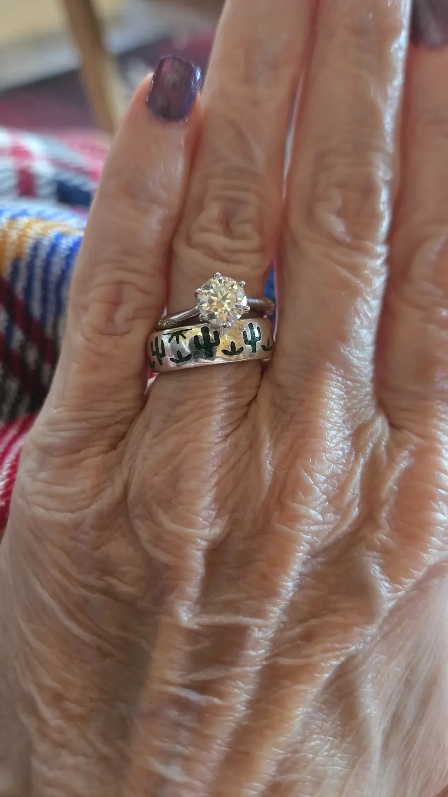 A close-up photo shows an elderly person's hand with wrinkled skin, displaying two rings on the ring finger: a silver band…