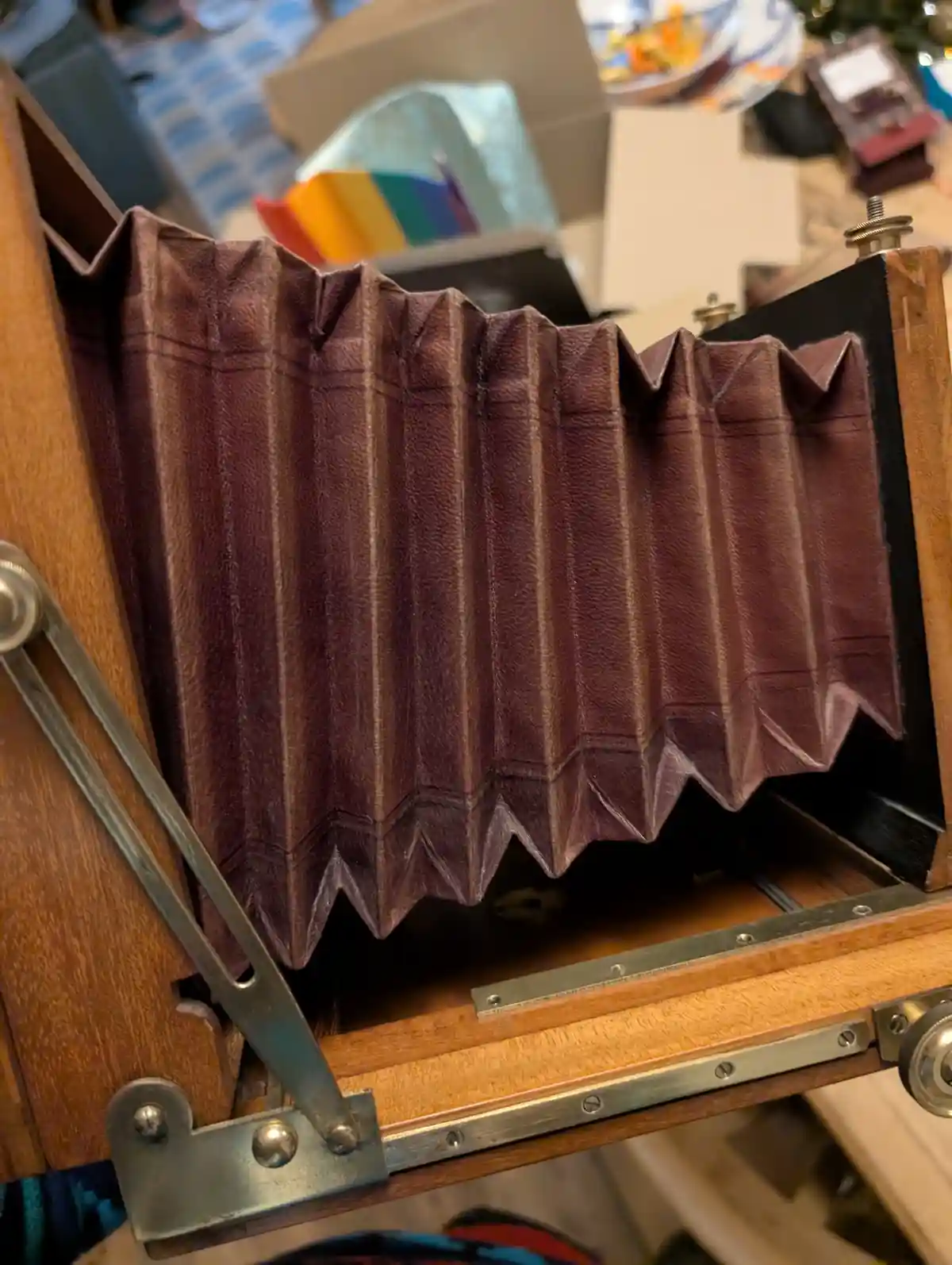 A close-up of a vintage wooden camera with a brown leather bellows partially extended, showing its accordion-like folds. The…