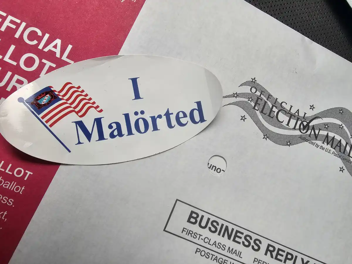 A close-up photo shows a white oval sticker with the text 'I Malörted' and a stylized American flag graphic placed on top of…
