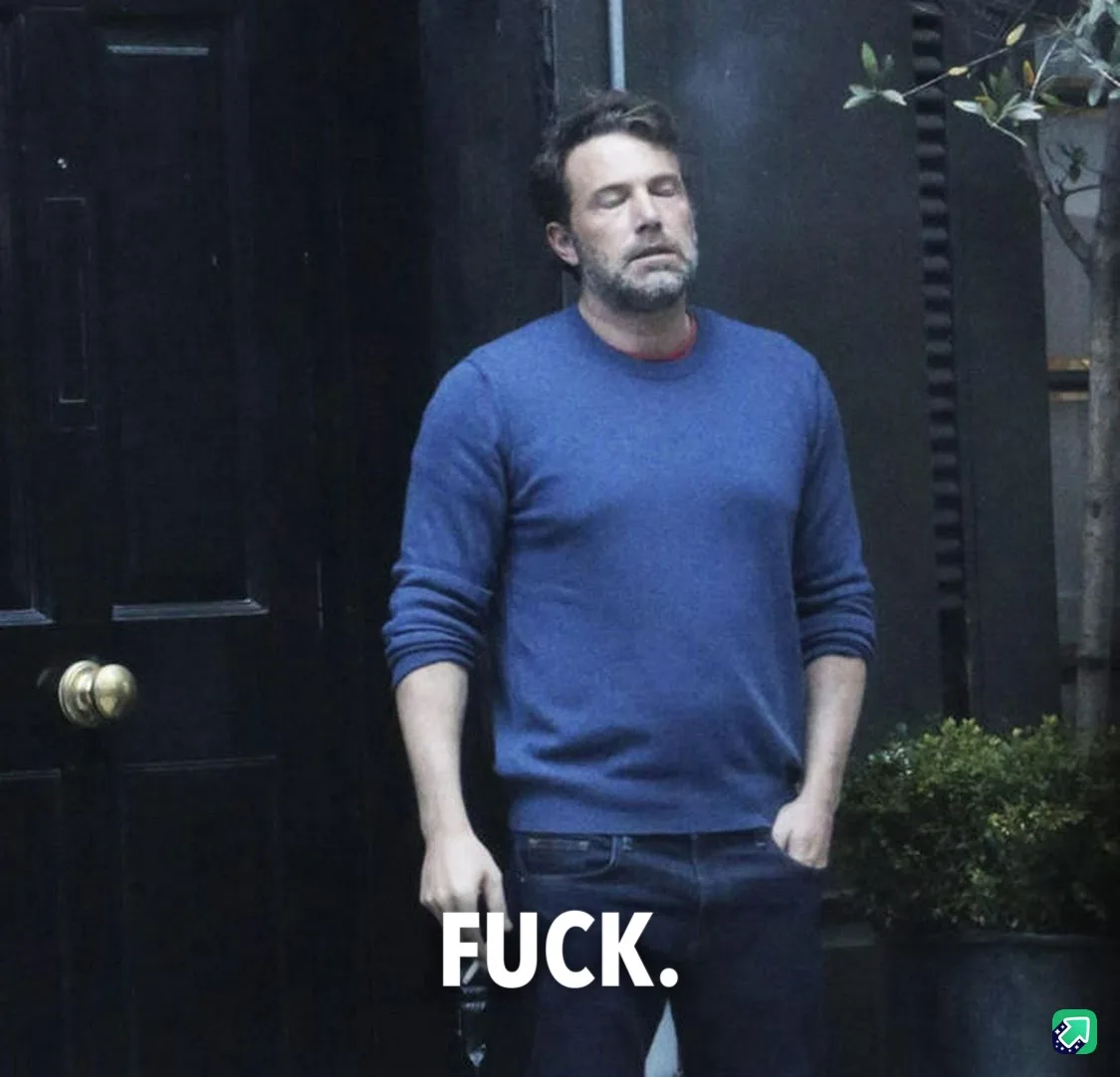 A man with a beard and short hair, wearing a blue sweater and jeans, stands outside a dark door with his eyes closed and…