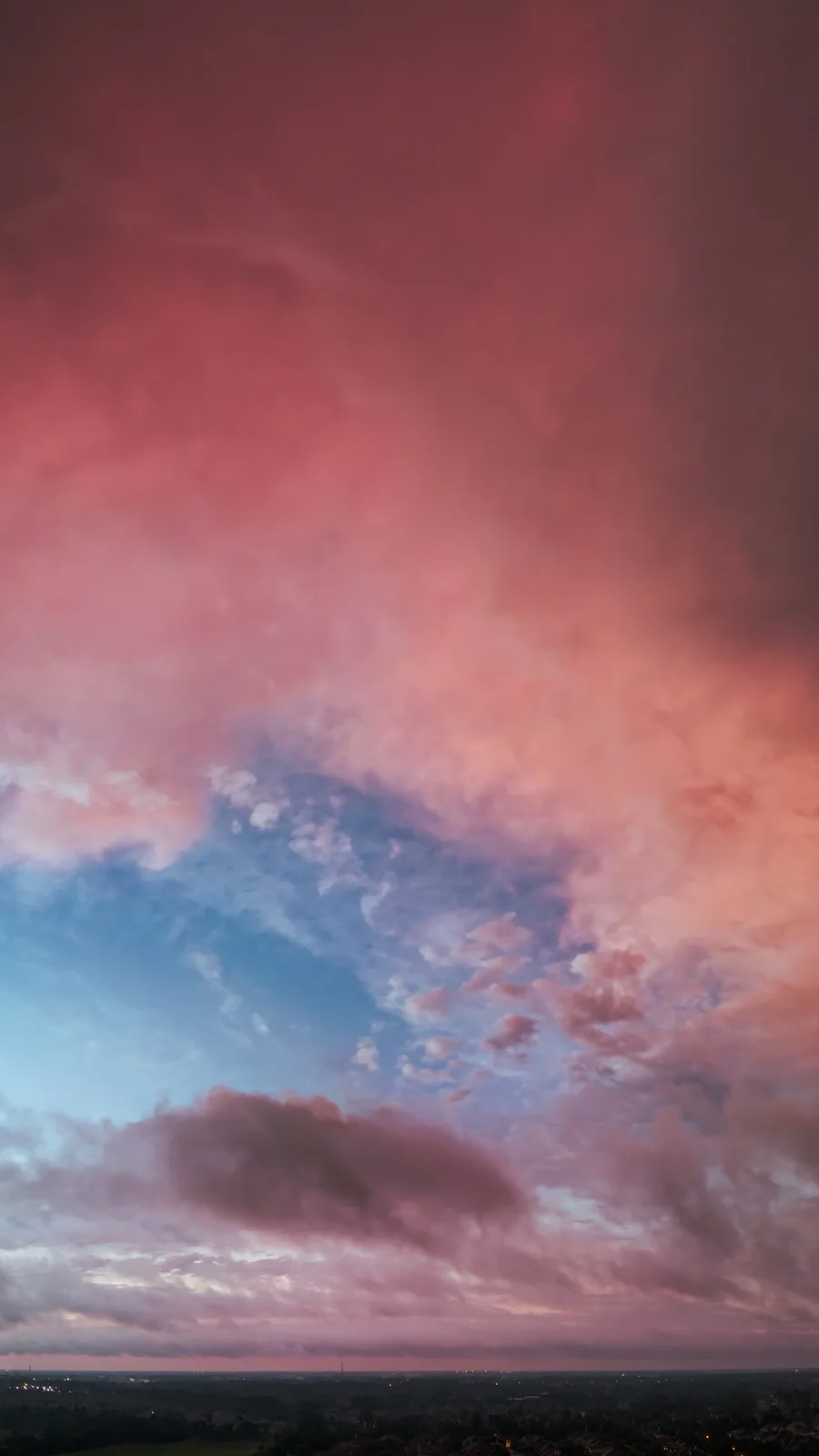 A dramatic sky with vibrant pink and orange clouds contrasting against a blue sky, overlooking a distant cityscape at dusk…