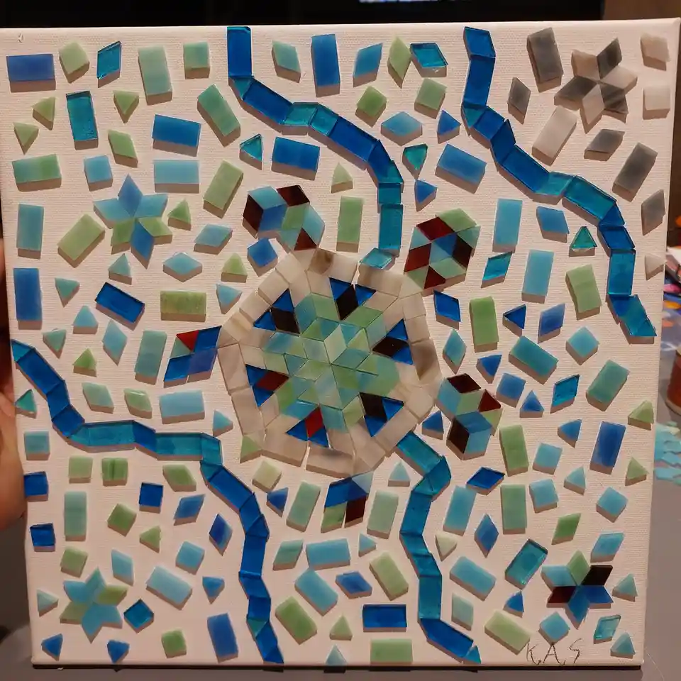 A hand holds a square canvas mosaic depicting a turtle made of blue, green, and white glass tiles, with the text 'i made…