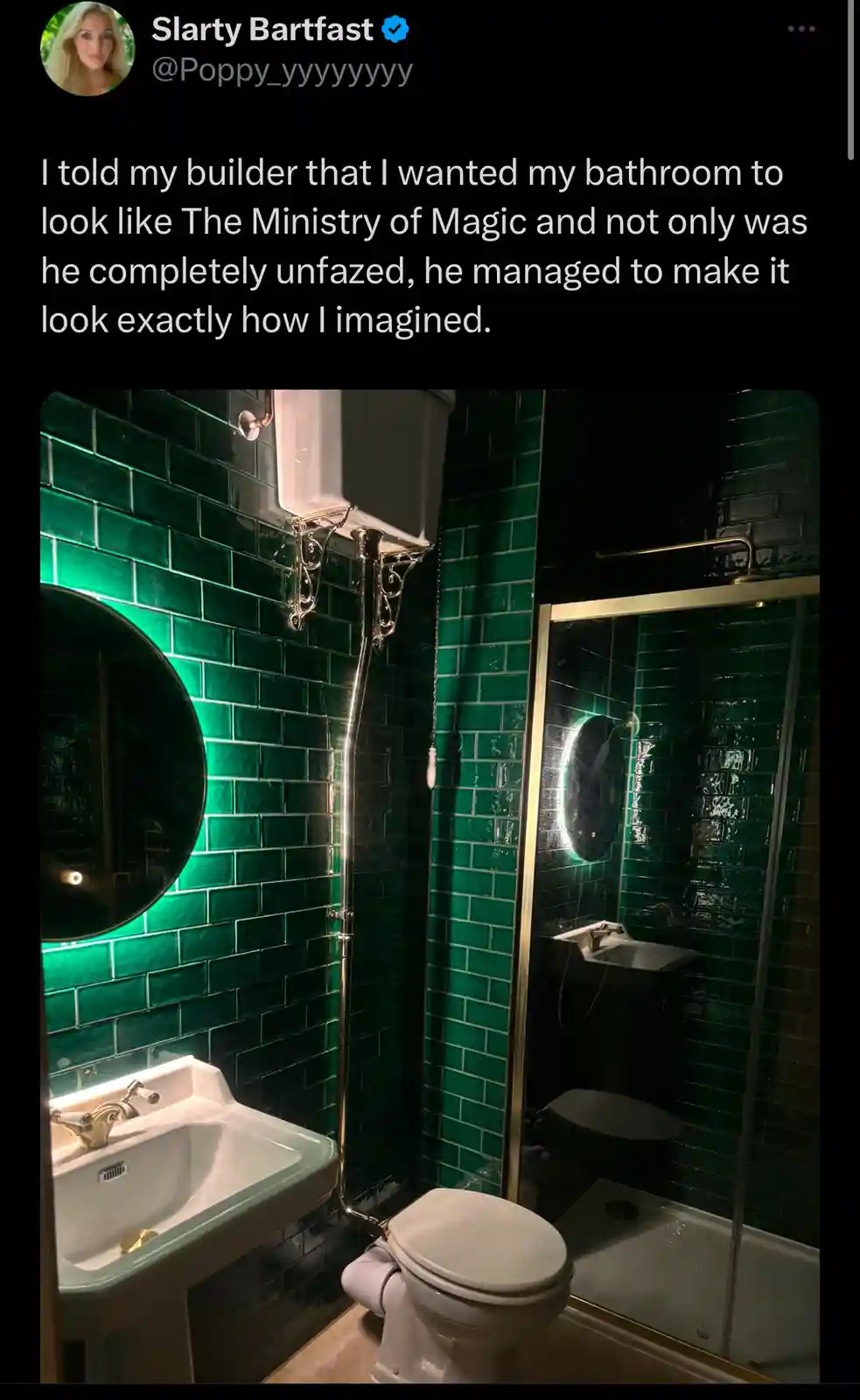 A bathroom with dark green subway tiles, a white sink, toilet, and shower, accented with gold fixtures and a round mirror…