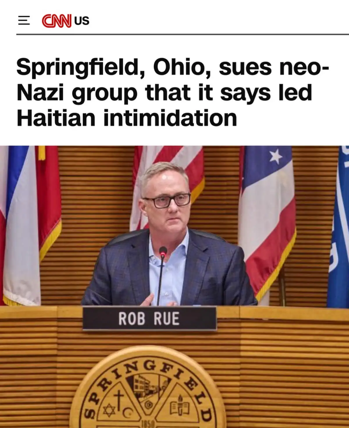 A screenshot of a CNN US news article header showing a man named Rob Rue speaking at a podium with the Springfield, Ohio…