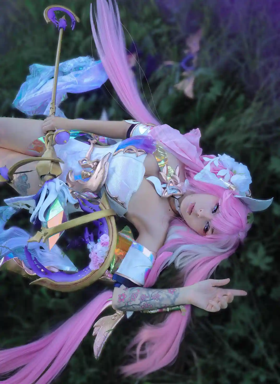 A person in a detailed cosplay of a character with long pink and white hair, wearing a white and gold outfit with floral…