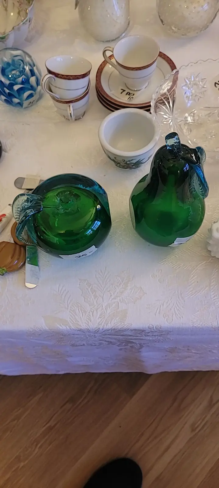 A photo of various vintage glassware and porcelain items on a white tablecloth, including two green glass pitchers with…