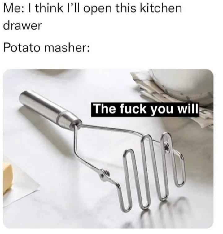 A stainless steel potato masher sits on a white countertop, with a block of butter and a white bowl partially visible in the…