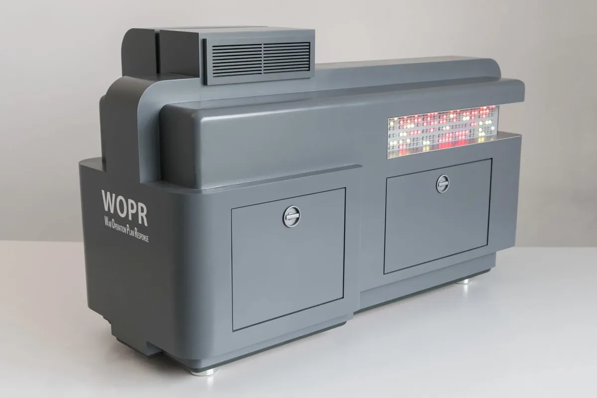 A gray, boxy computer console labeled 'WOPR War Operation Plan Response' with a red and white LED display panel on top and…