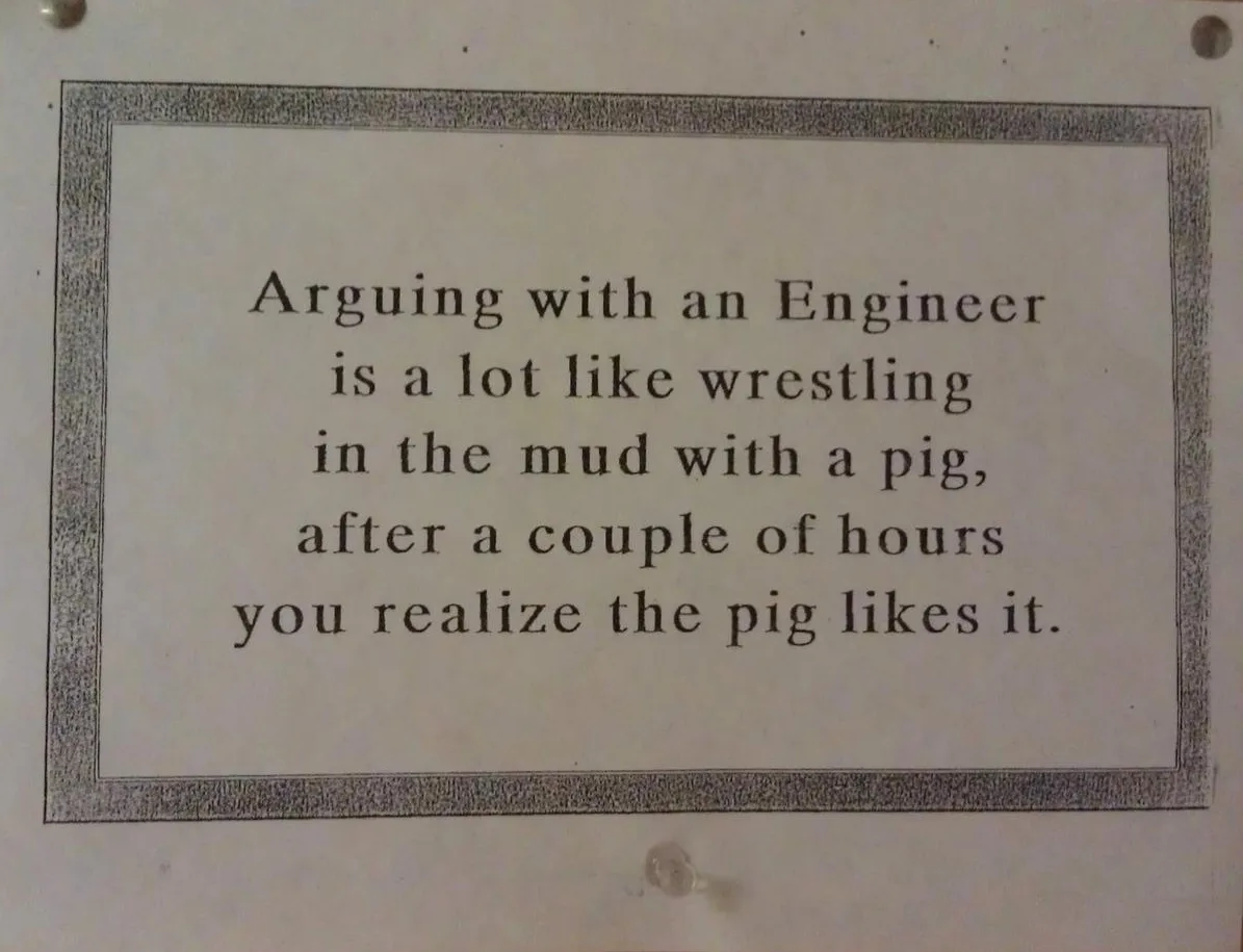 A printed sign with a black border and serif font text that reads: 'Arguing with an Engineer is a lot like wrestling in the…
