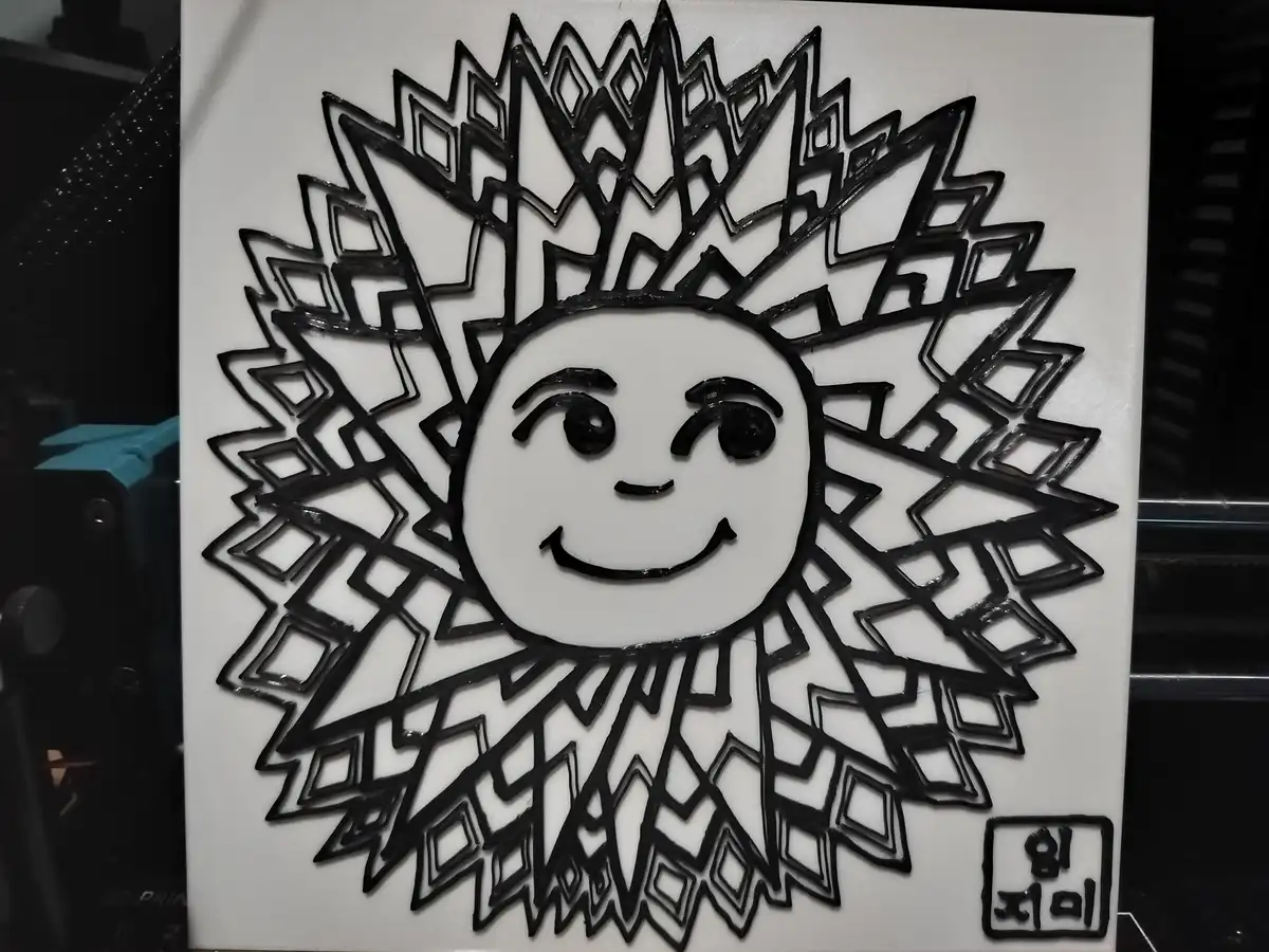 A 3D-printed black-and-white sun illustration with a smiling face and geometric rays, displayed on a white square panel. The…