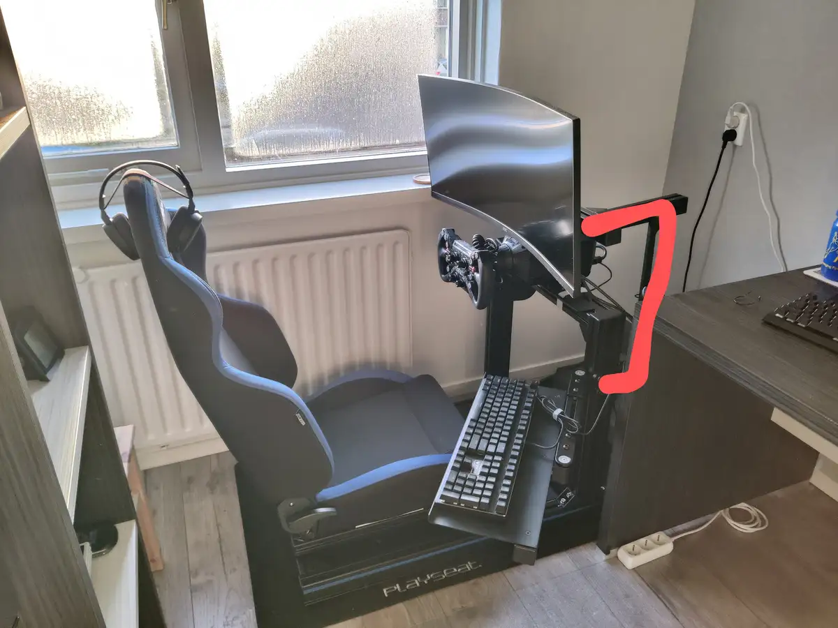 A photo of a high-end racing simulator setup featuring a black and blue Playseat racing chair with a headset hanging on the…