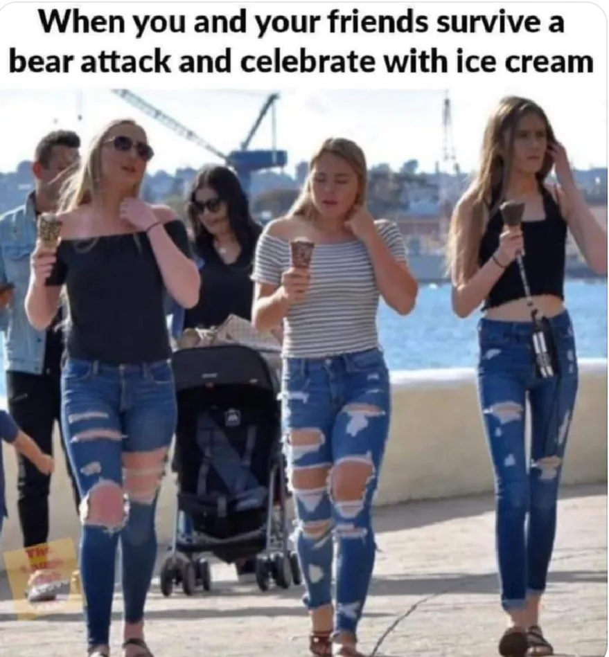 A group of young women, dressed in ripped jeans and casual summer clothes, are walking along a waterfront while holding ice…