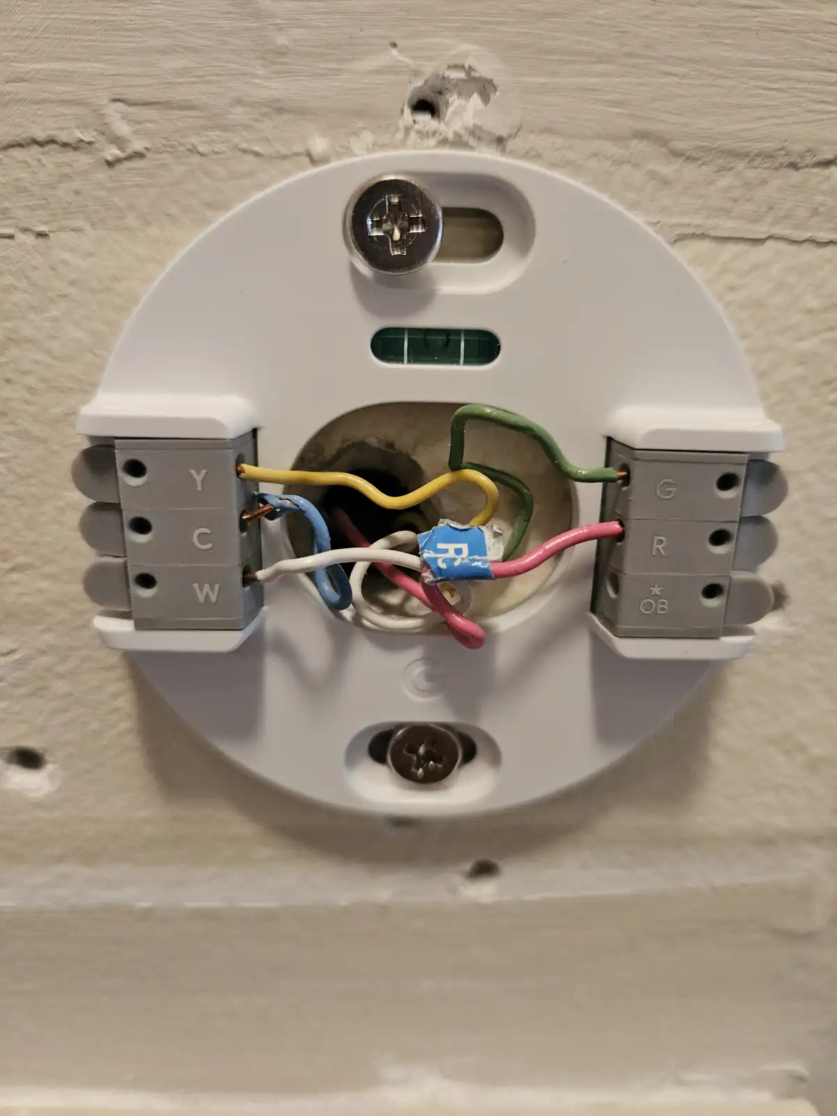 A close-up photo shows the back of a white electrical device mounted on a textured wall, with exposed wires (yellow, green…