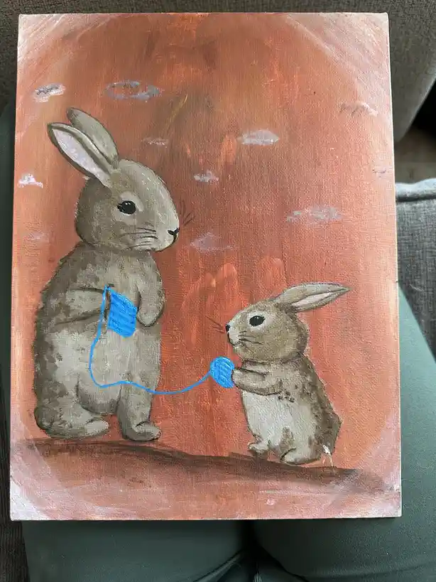 A hand-painted canvas depicts two brown rabbits against an orange sky with white clouds; the larger rabbit holds a blue…