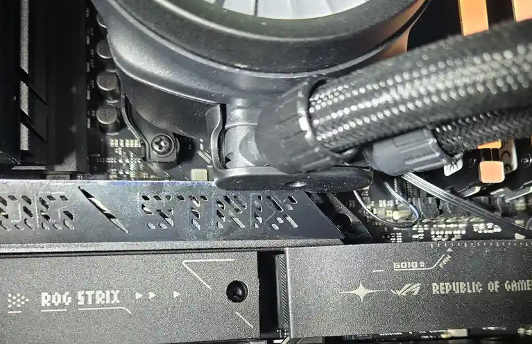 A close-up photo of a computer's internal hardware, showing a black ROG STRIX motherboard with visible screws, circuitry…