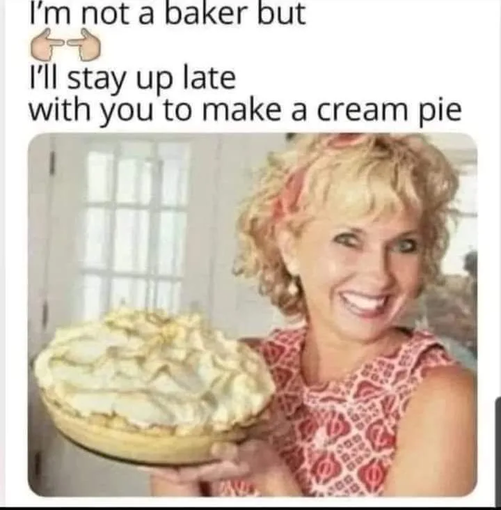 A woman with curly blonde hair and a red patterned top is smiling broadly while holding a cream pie with whipped cream…