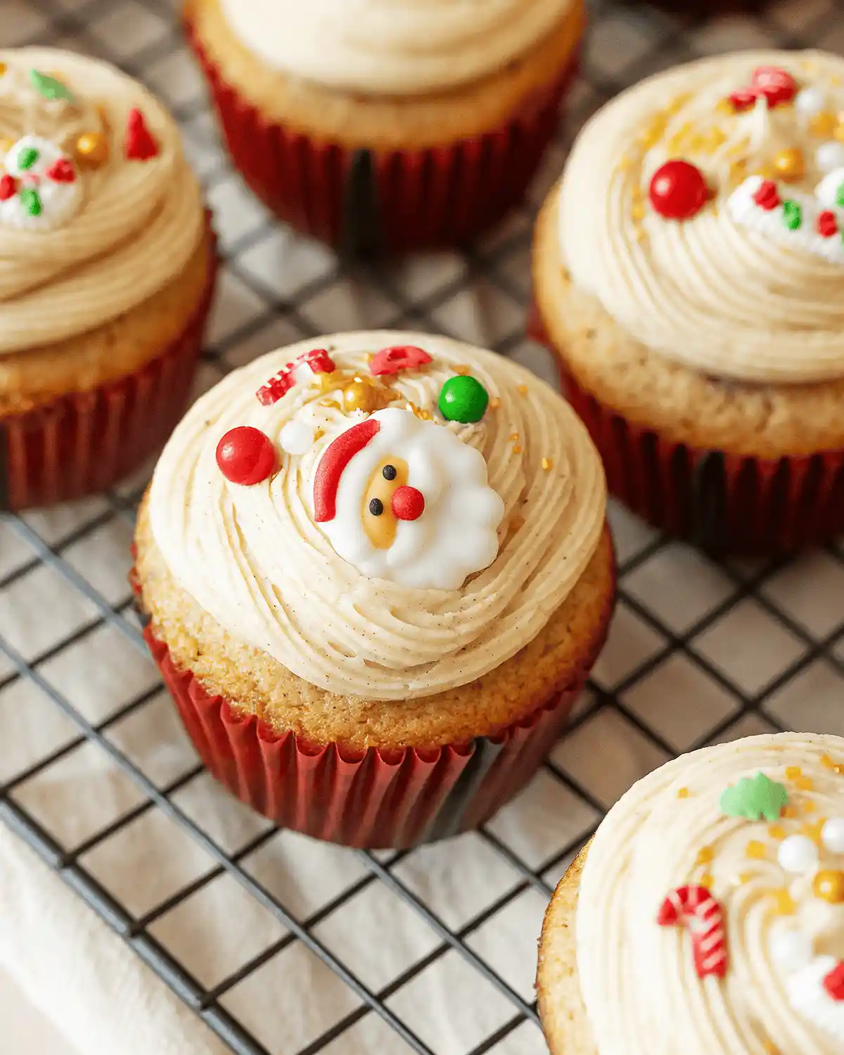 Several cupcakes with light brown frosting sit on a wire cooling rack, each decorated with festive sprinkles. The central…