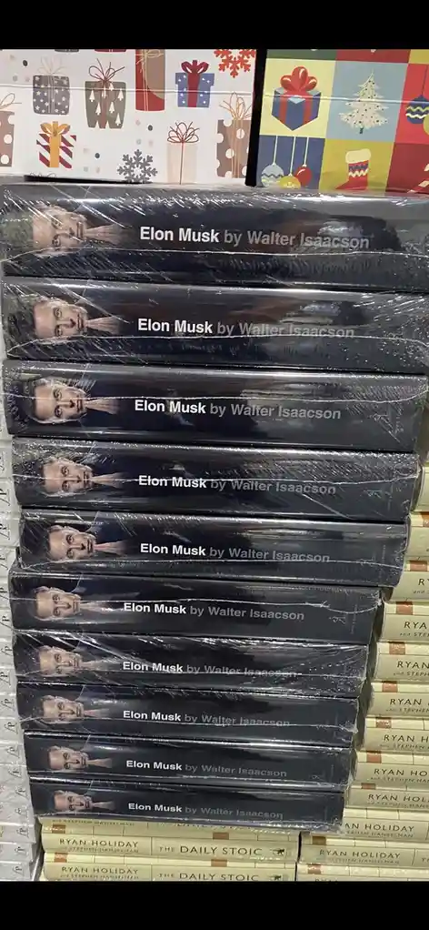 A tall stack of identical 'Elon Musk by Walter Isaacson' biographies, wrapped in plastic, sits on a bookstore shelf. Behind…