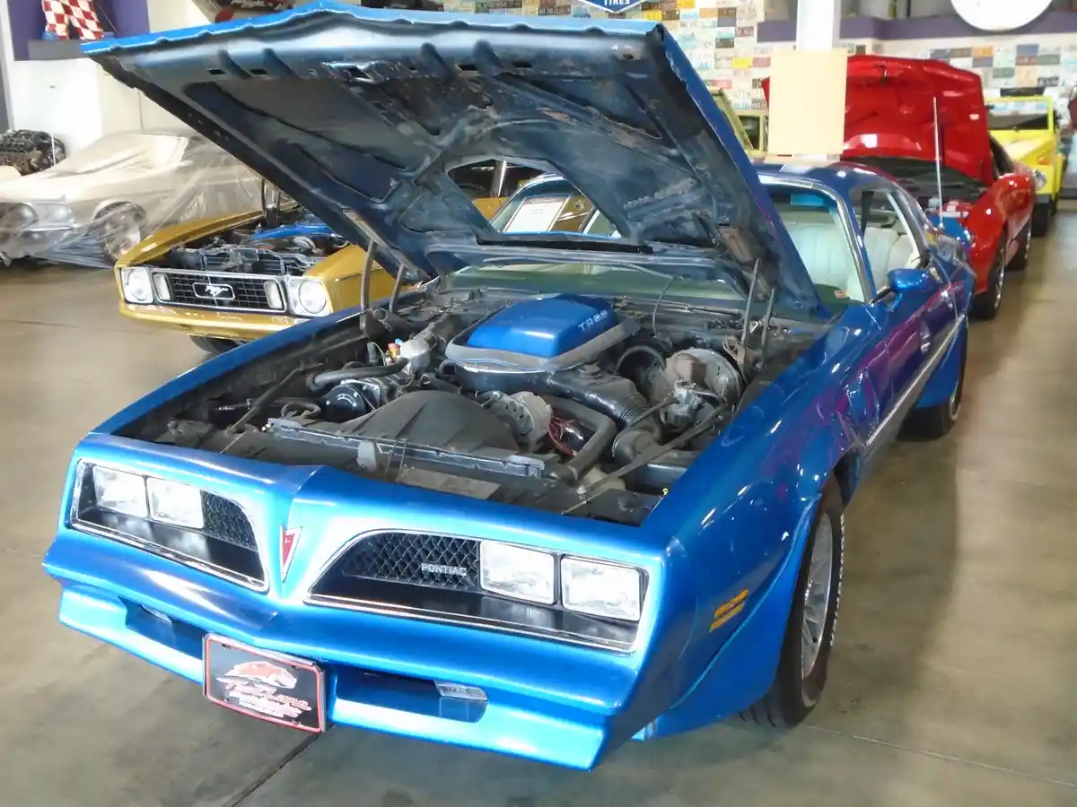 a blue pontiac trans am with its hood open, revealing the engine, is parked in a car showroom with other classic cars in the…