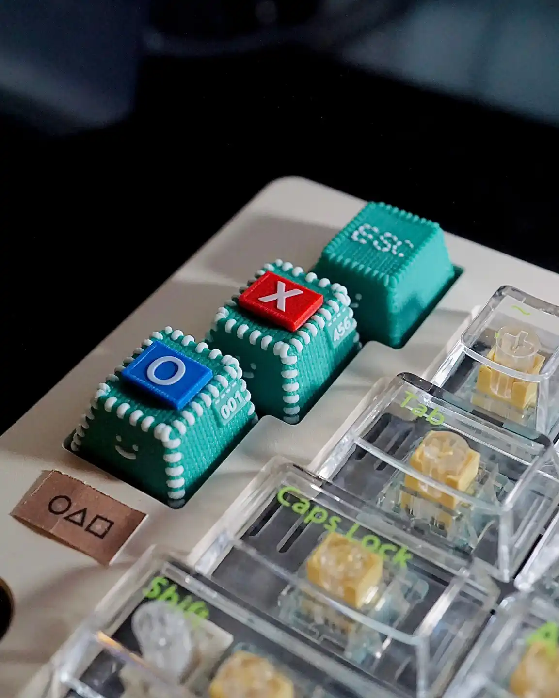 A close-up photo of a keyboard with three custom teal keycaps featuring white piped edges and smiley faces, one labeled 'O'…