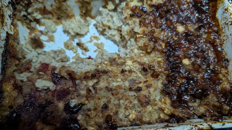 A close-up photo shows a partially eaten casserole dish with a golden-brown, crispy top layer and visible crumbs and sauce…