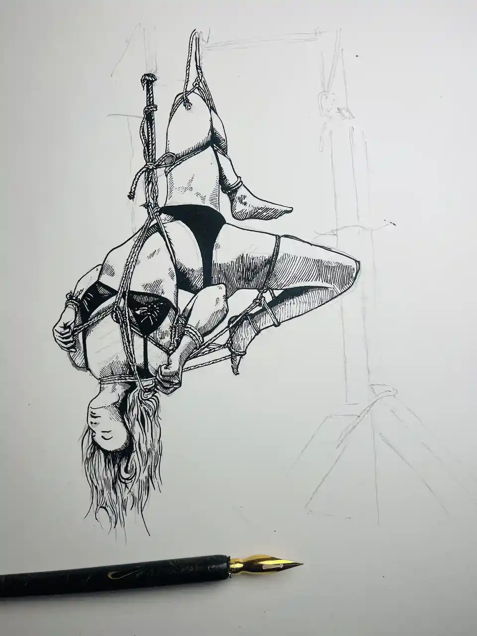 A black-and-white ink drawing on paper shows a person suspended upside down in a complex rope bondage pose, wearing lingerie…