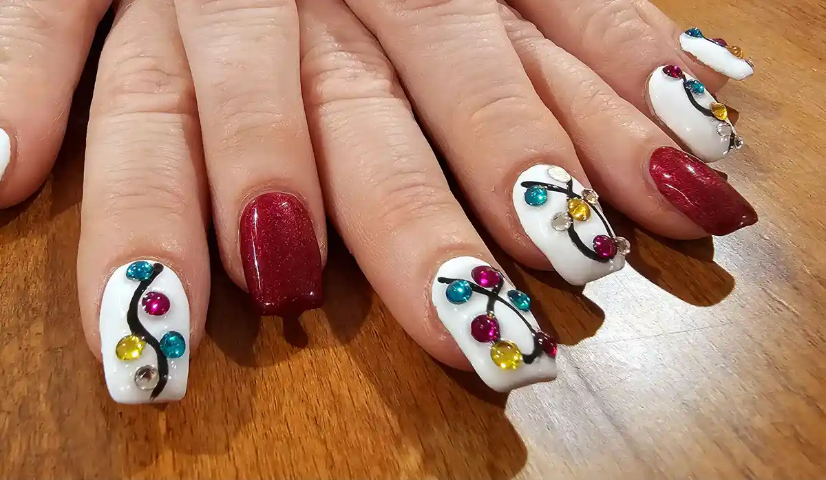 A close-up of a person's hands resting on a wooden surface, showcasing elaborately decorated fingernails. Several nails are…