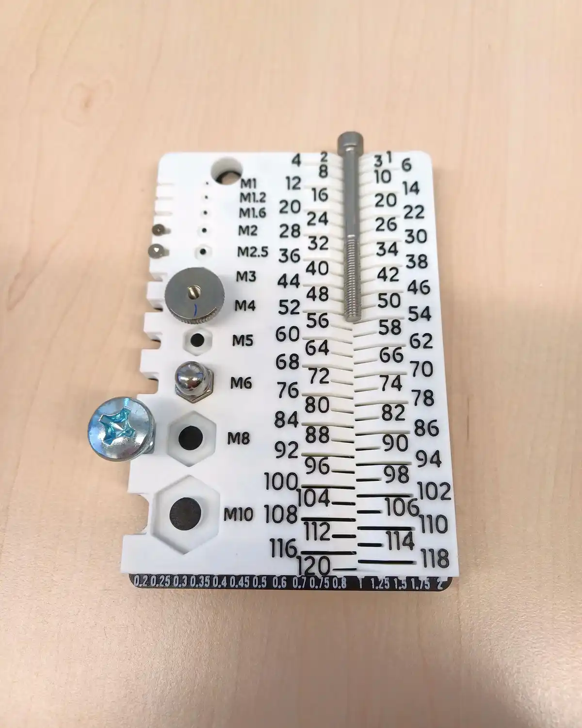 A white plastic screw gauge chart with various screw sizes labeled, including M1, M2, M3, M4, M5, M6, M8, and M10, with…