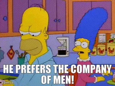 The image shows Homer Simpson in a kitchen, holding a small dark object while Marge Simpson stands beside him looking…