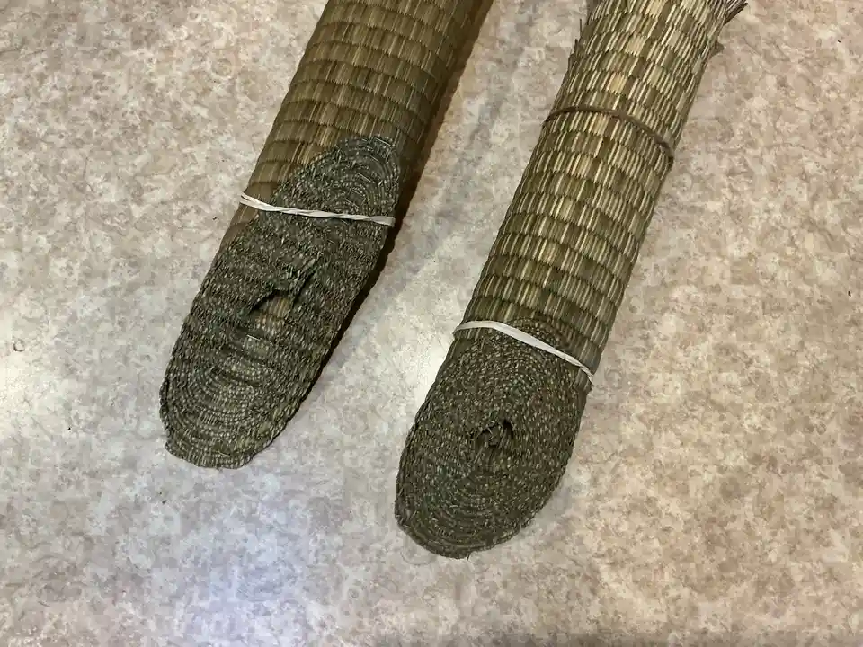 Two rolled-up, woven straw mats lie side by side on a speckled countertop, each tied with a rubber band. The mat on the left…