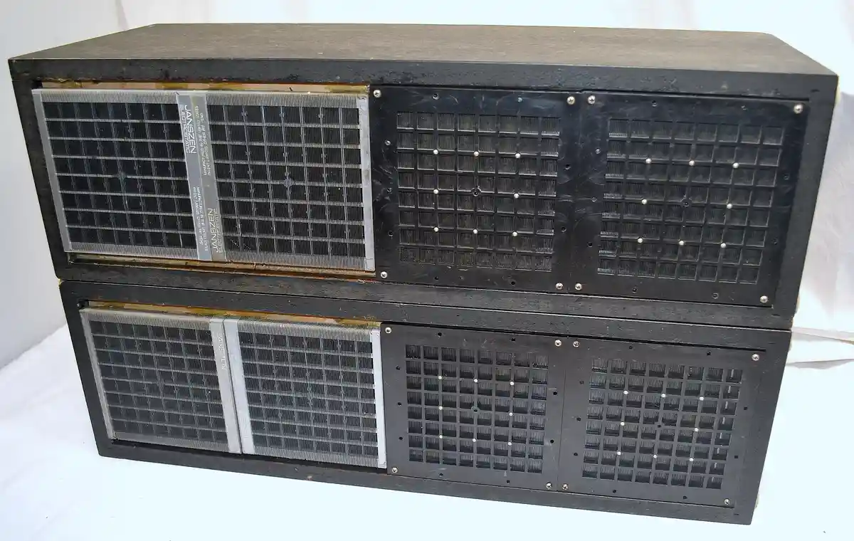Two stacked, black, boxy Janszen electrostatic air purifiers with visible metal grilles and labels, sitting on a white…