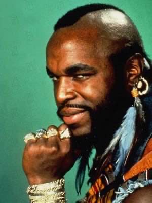 a man with a shaved head, beard, and feathered earring poses with his hand near his chin, wearing multiple rings and…