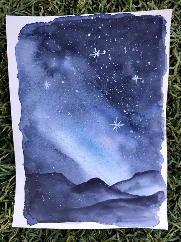 A watercolor painting on white paper depicts a starry night sky with a gradient from dark blue to light blue, featuring…