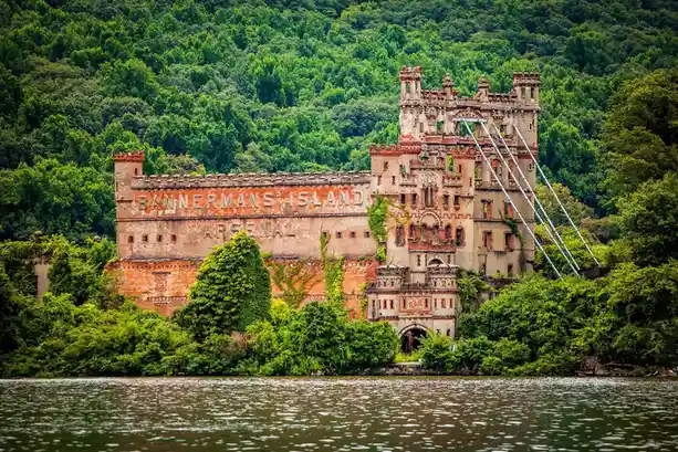 An abandoned, ivy-covered castle-like structure with 'BANNERMAN'S ISLAND ARSENAL' painted on its brick facade, situated on a…