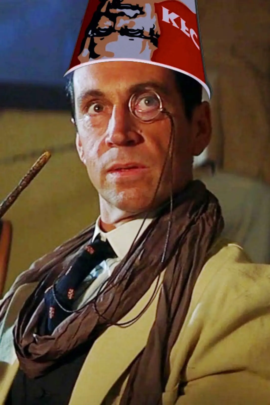 A man with round glasses and a scarf wears a red KFC bucket as a hat, looking shocked. The bucket has the KFC logo and…