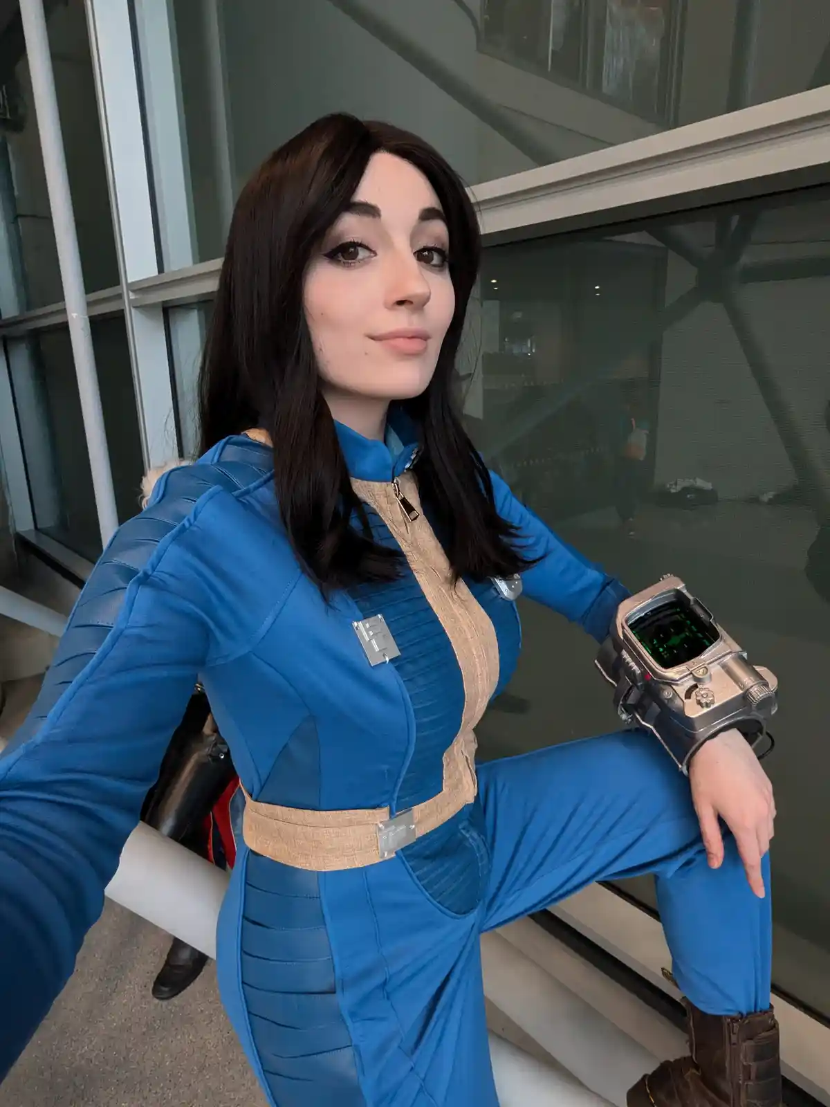 A person in a blue Vault Dweller cosplay from Fallout, complete with a wrist-mounted Pip-Boy device, poses confidently while…