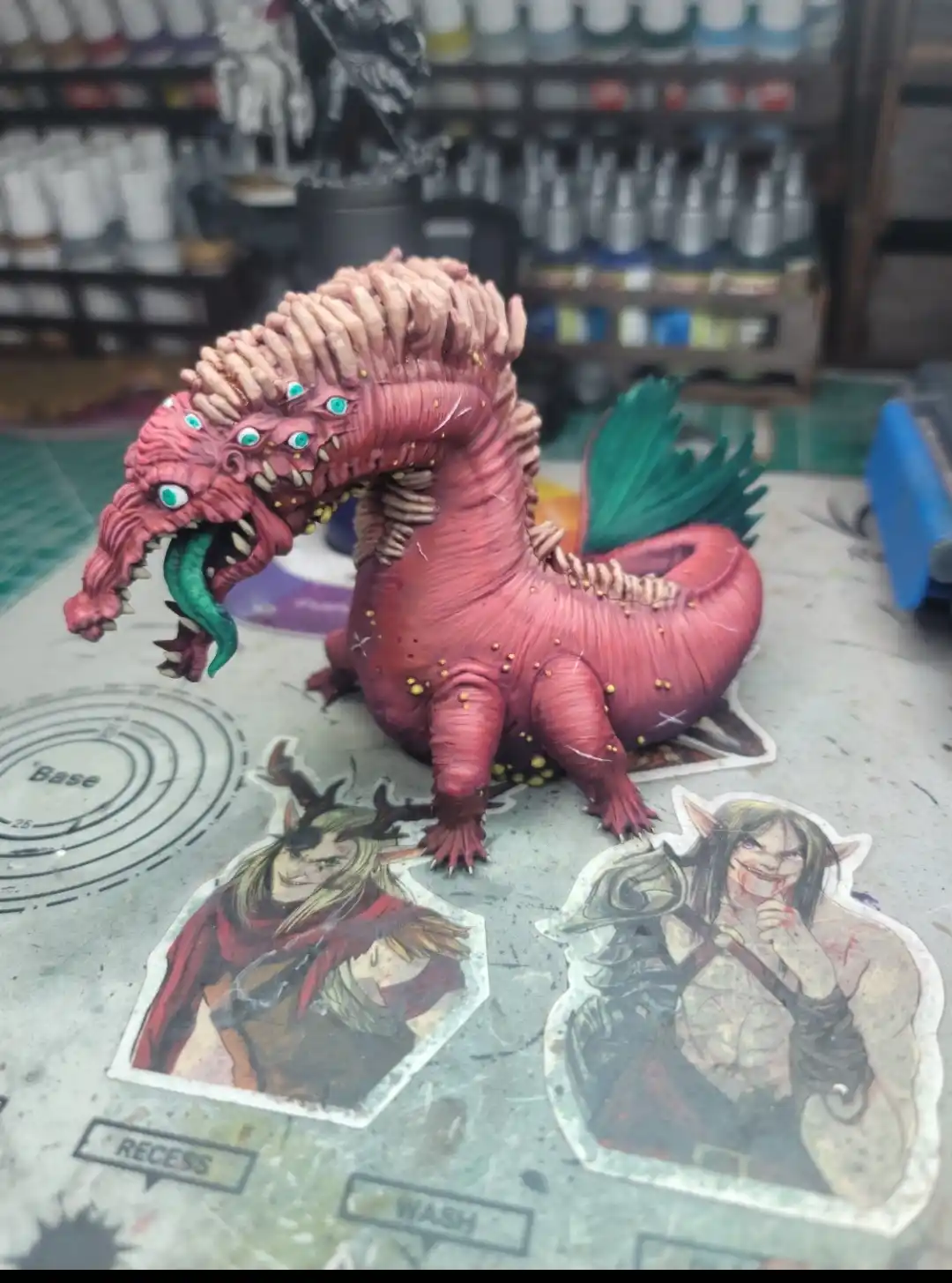 A highly detailed, hand-painted pink dragon figurine with multiple turquoise eyes, a green tongue, and spiky ridges sits on…