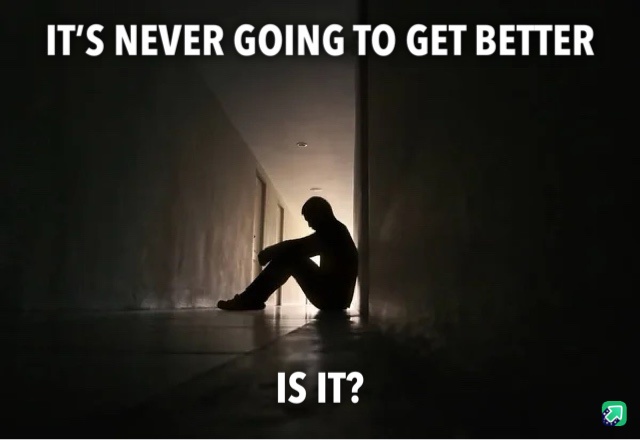 A dark, atmospheric image shows the silhouette of a person sitting alone on the floor in a dimly lit hallway, hunched over…