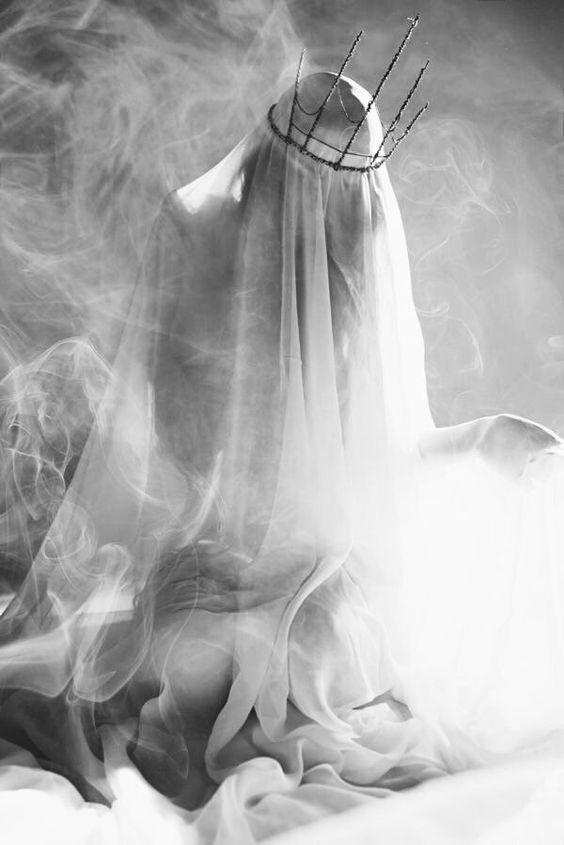A black-and-white image shows a figure draped in a flowing white veil, with a crown of thorns resting on their head…