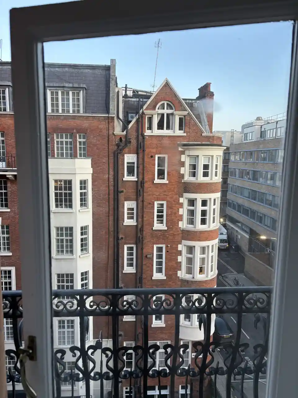 A photo taken from inside a room looking out a window at a red brick building with white-trimmed windows and a decorative…