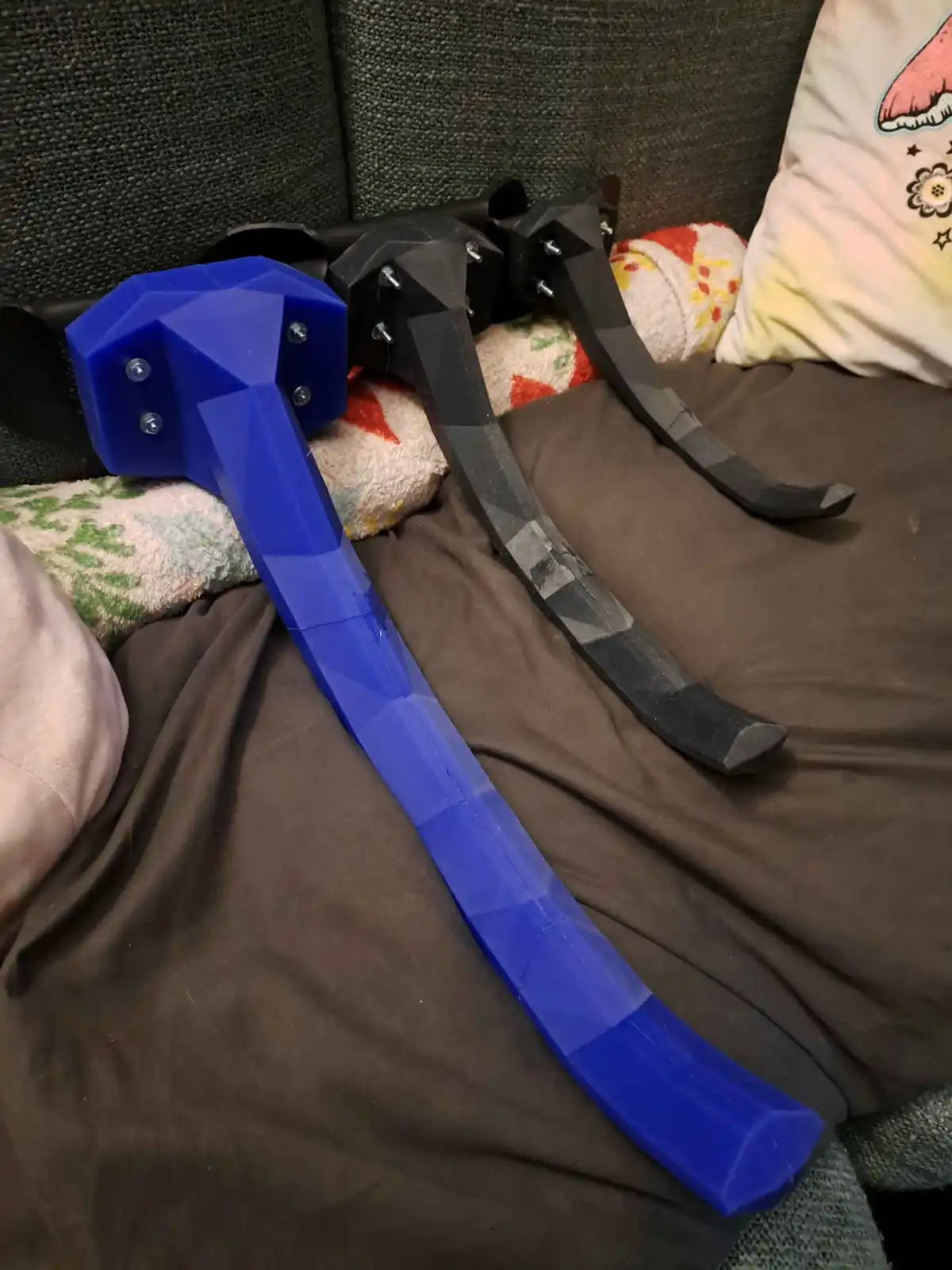 A handmade pickaxe and sword with a low-poly, blocky design, resembling Minecraft items, are resting on a couch. The pickaxe…
