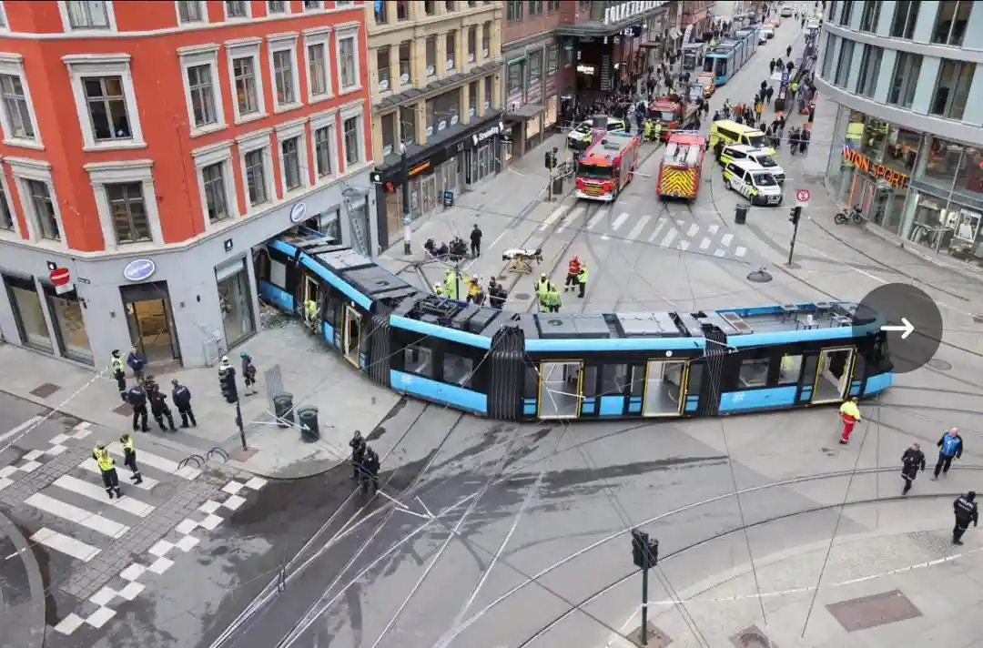 An aerial view shows a blue and black tram that has crashed into a building corner, bending sharply into an unnatural curve…