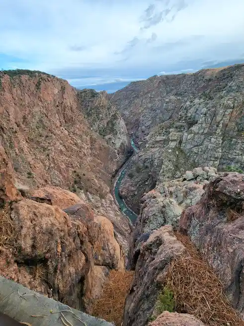 A scenic view from a high vantage point overlooking a deep, narrow canyon with steep, rocky walls. A river flows through the…