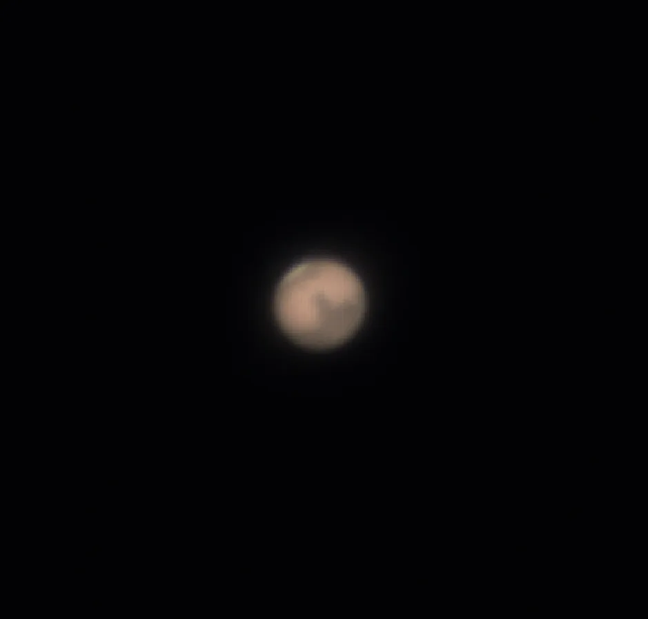 A blurry, low-resolution image shows a pale, orange-brown circular object resembling a planet or moon against a black…
