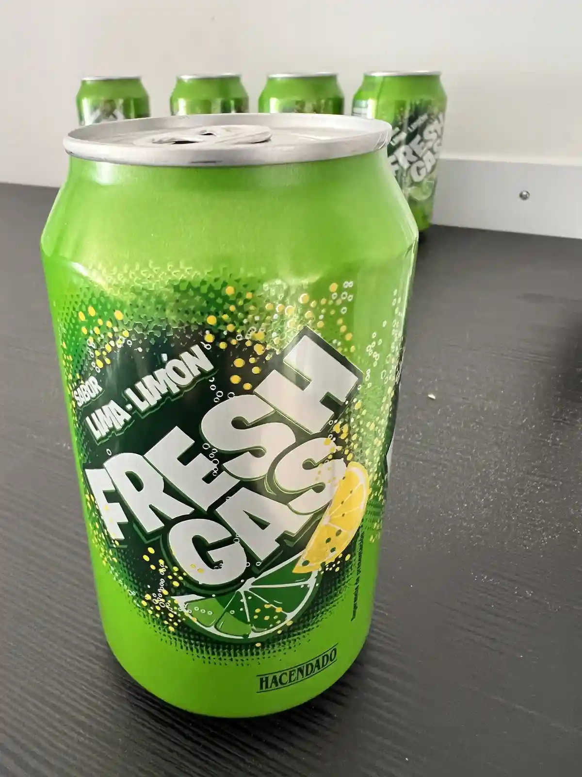 A bright green Hacendado soda can labeled 'Sabor Lima-Limon' and 'Fresh Cash' sits in the foreground on a dark table, with…