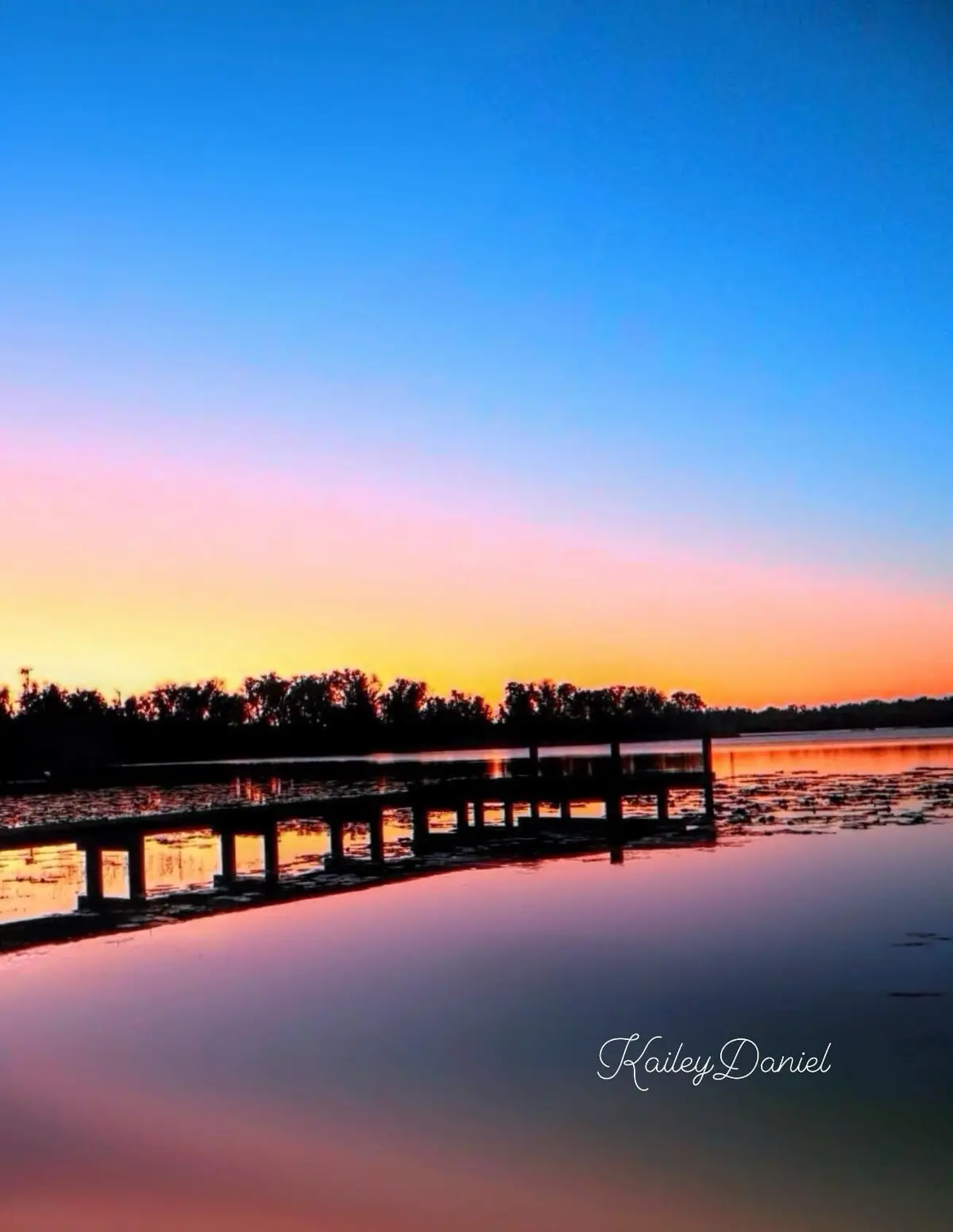 A serene sunset photo shows a wooden pier extending into calm water, reflecting the sky's gradient from deep blue to orange…