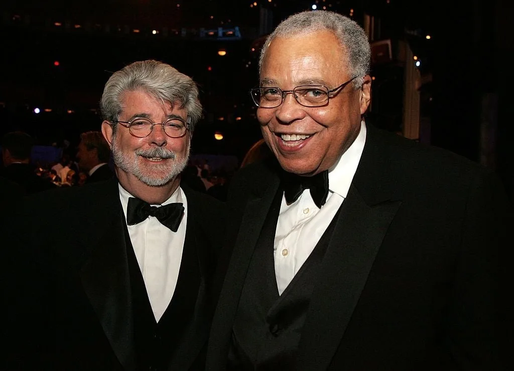 two men in tuxedos, one with gray hair and glasses, the other with gray hair and glasses, both smiling at the camera. the…